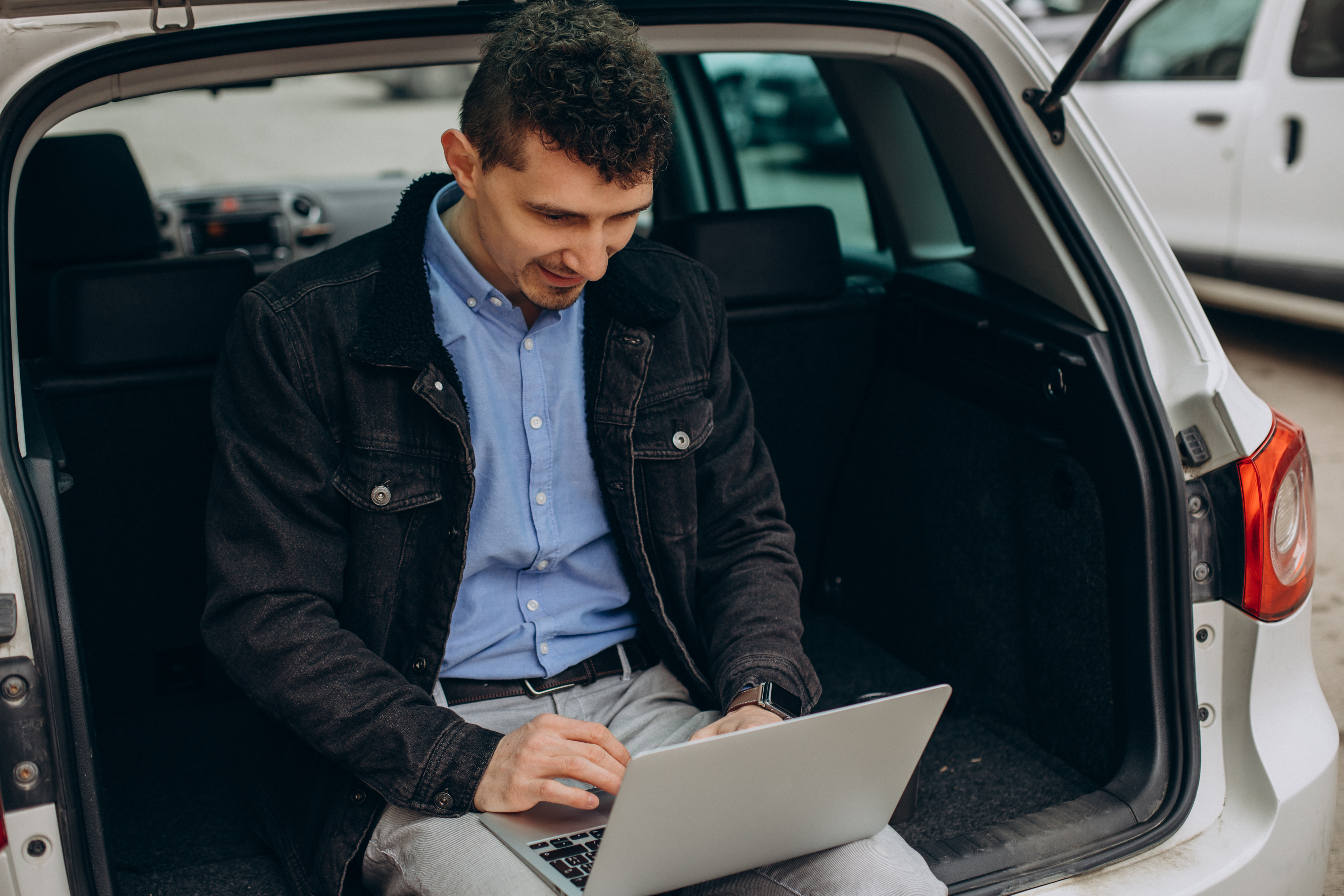 man-sitting-trunk-his-car-working-computer.jpg